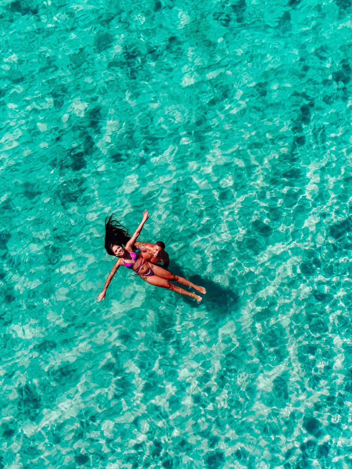 Vista aérea de casal boiando na água turquesa em Arraial do Cabo