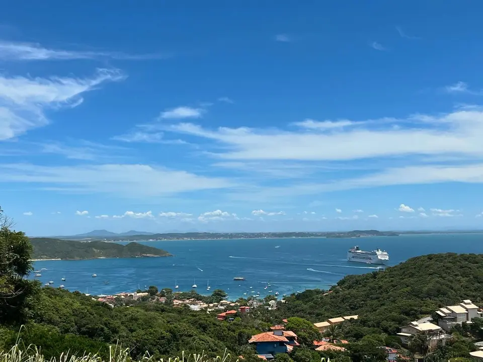Vista panorâmica do alto da baía de João Fernandes com águas azul-turquesa, casas de luxo e a linha costeira de Búzios ao fundo.