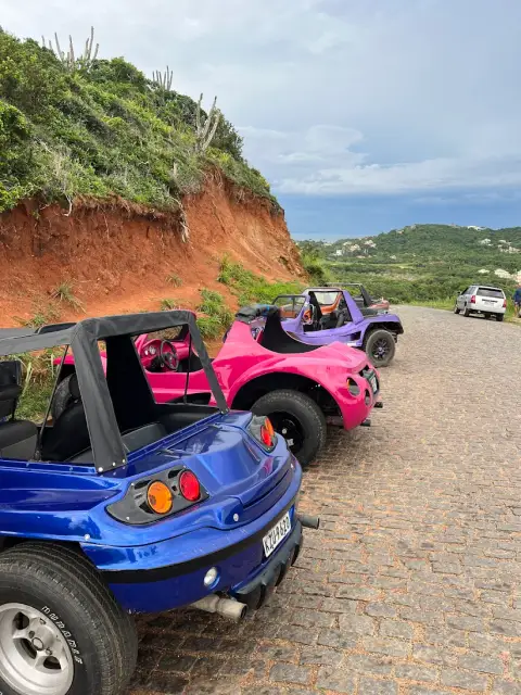 Um turista sorrindo enquanto olha para um smartphone com a tela de confirmação da Buggy Búzios, com a costa de Búzios ao fundo.