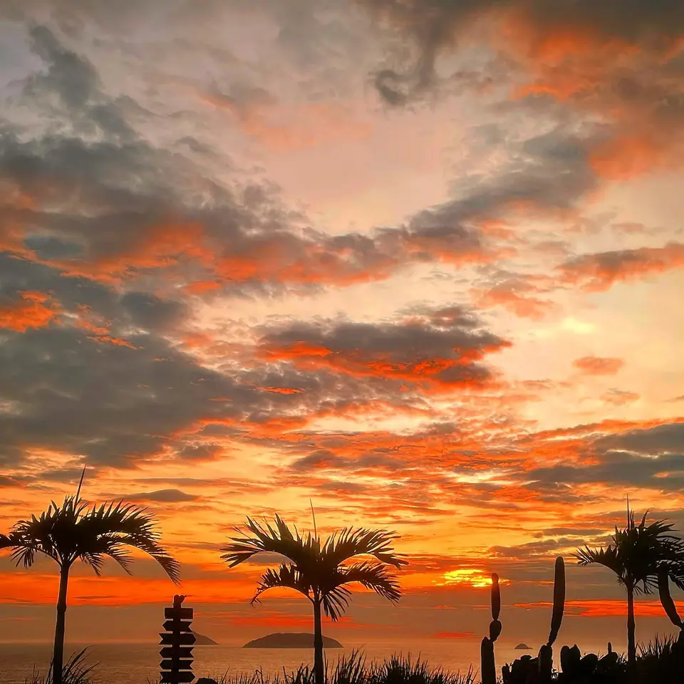 A panoramic view of the golden sun sinking below the ocean horizon, casting a deep orange glow over the cliffs and beaches of Búzios.