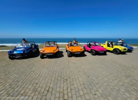 Comboio de buggies coloridos de praia rodando juntos por uma estrada costeira em Búzios em um dia ensolarado.